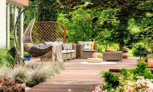 Un acogedor rincón en un jardín de verano, con muebles de mimbre, una silla colgante y vegetación exuberante.