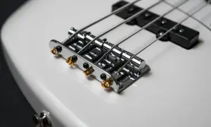 Błyszcząca, biała gitara basowa elektryczna z chromowanym mostkiem i złotymi detalami.