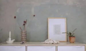 Un tavolino con candela, vaso di fiori secchi, quadro e corda. Sembra la preparazione calce per imbiancare, con un tocco artistico.