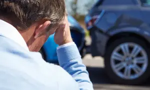 Mężczyzna zmartwiony po wypadku samochodowym, widoczne uszkodzone auta.