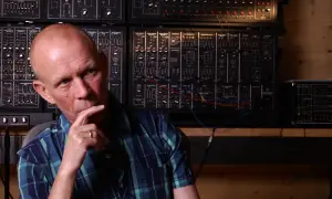 Vincent Clarke, zamyślony, siedzi przed ścianą syntezatorów.