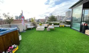 Terraza con césped artificial verde, jacuzzi, muebles de exterior y vistas urbanas. Ideal para aprender como limpiar césped artificial terraza.