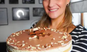 Lächelnde Frau präsentiert eine köstliche Kinderriegel Torte, dekoriert mit Schokostückchen und ganzen Riegeln.