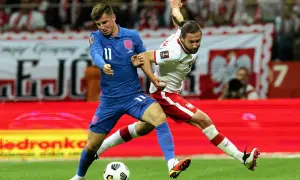 Piłkarz Anglii w niebieskiej koszulce walczy o piłkę z zawodnikiem Polski w białej. Emocjonujący mecz Anglia Polska.