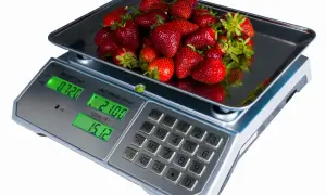 Kobiałka pełna soczystych truskawek waży się na wadze cyfrowej, pokazując 0.720 kg.