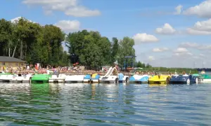 Słoneczny dzień nad jeziorem w Powidzu. Rząd kolorowych rowerów wodnych czeka na plażowiczów.