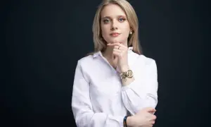 Kobieta w białej koszuli, z ręką na podbródku, pokazuje, jak zrobić zdjęcie biznesowe w domu.