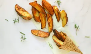 Patate al forno dorate e croccanti, profumate al rosmarino, servite su carta da forno e in un cono di bambù.