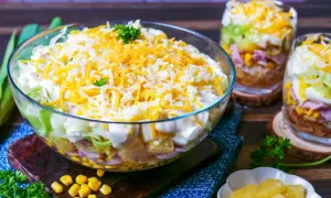 Schichtsalat rezept: Ein bunter Salat in einer Glasschüssel, geschichtet mit Mais, Schinken, Ei, Lauch und Käse.