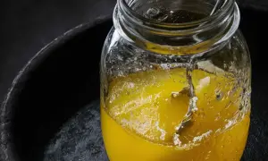 Słoik z płynnym, żółtym tłuszczem, być może ghee, na ciemnym tle. Czy oliwa z oliwek jest zdrowa? To pytanie nurtuje wielu.