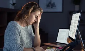 Kobieta z ręką na czole, wyrażająca niechęć do pracy przy biurku w nocy.