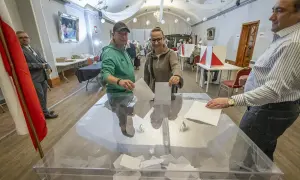 Ludzie oddają głosy w lokalu wyborczym, korzystając z czynnego prawa wyborczego. W tle widać flagę Polski.