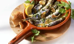 Leckeres Sardinen Rezept in einer Terracotta-Pfanne mit Zitrone, Knoblauch und Petersilie, dazu Brot.