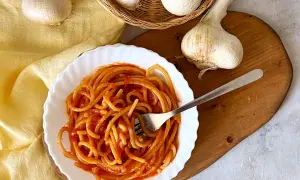 Piatto di pici all'aglione fumanti, con aglio fresco in primo piano. Un classico della cucina toscana.