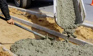 Wylewanie świeżego betonu z betoniarki. Robotnik łopatą rozprowadza masę, która zawiera cement i kruszywo.