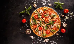 Krojona pizza z pomidorami, pieczarkami i bazylią na czarnym tle, otoczona składnikami.