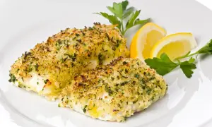 Delizioso merluzzo al forno con crosta dorata di pangrattato ed erbe aromatiche, guarnito con spicchi di limone e prezzemolo fresco.