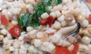 En närbild på en tallrik med fregola pasta, musslor och tärnad tomat, toppad med färsk persilja.