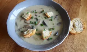 Un réconfortant velouté de champignon, garni de croûtons dorés et de ciboulette fraîche, servi dans un bol bleu sur une table en bois.