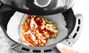 Odgrzewanie pizzy w piekarniku beztłuszczowym. Kawałek pizzy z kurczakiem, serem i sosami w koszu frytkownicy.