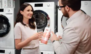 Kobieta i mężczyzna rozmawiają o produktach do prania Miele, stojąc przed nowoczesnymi pralkami.
