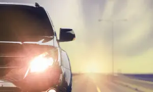 Las luces del coche brillan intensamente al amanecer en una carretera desierta.
