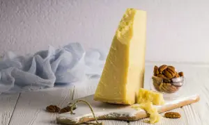 Kawałek twardego sera, który wygląda jak parmezan, leży na desce z orzechami pekan.