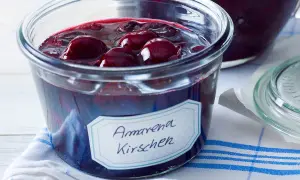 Ein Glas mit Amarena Kirschen, perfekt für ein Amarena Kirschen Rezept. Die dunklen Früchte schwimmen in Sirup.