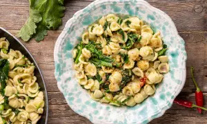 Orecchiette con cime di rapa, la ricetta originale pugliese, servite in un piatto decorato, con peperoncini rossi e foglie di rapa sullo sfondo.