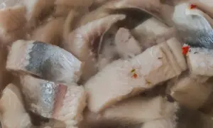 Kawałki kiszonych śledzi w zalewie, z widocznymi fragmentami skórki i przyprawami.
