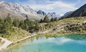Sentier de randonnée longeant un lac turquoise dans le Val d'Hérens, avec des montagnes majestueuses en arrière-plan.