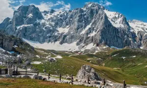 Majestuosas montañas nevadas en los Picos de Europa, cerca de Llanes. Un camino de piedra y madera serpentea por prados verdes salpicados de nieve.