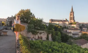 Donna passeggia su un muro a Saint-Émilion, con il villaggio e la sua chiesa in lontananza.
