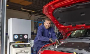 Mekaniker arbetar med ac i bilen. Han kopplar slangar till bilens AC-system vid en serviceenhet.