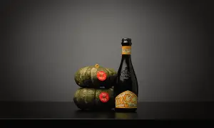 Una bottiglia di birra alla zucca accanto a due zucche impilate.