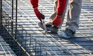 Budowlaniec wiąże zbrojenie, szacując, ile stali na fundament 100m2 będzie potrzebne.