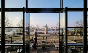 Blick durch offene Glastüren auf den Hamburger Hafen mit dem alten Elbtor und Kränen. Eine Frau genießt die Aussicht, perfekt für einen Stintfang Hamburg.
