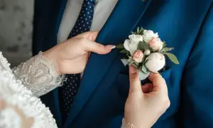 Les mains de Caroline ajustent la boutonnière sur le costume bleu du marié. Un moment tendre avant leur mariage à l'hôtel.