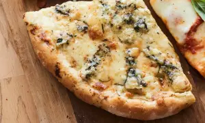 Une part de pizza 4 fromages, avec sa croûte dorée et son mélange de fromages fondus, sur une planche en bois.