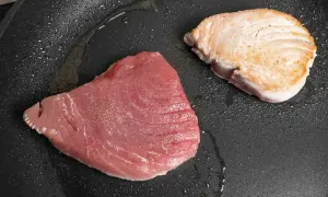 Zwei Thunfischfilets in einer Pfanne: eines roh und rosa, das andere leicht angebraten und goldbraun.