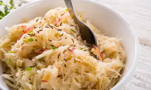 Frisch zubereitetes Sauerkraut mit Kümmel und Apfelstücken in einer weißen Schüssel, bereit zum Servieren.
