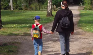Dzieci autystyczne lubią spacery i poczucie bezpieczeństwa. Chłopiec z plecakiem idzie za rękę z kobietą po ścieżce w parku.
