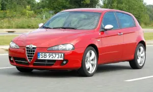 Czerwona Alfa Romeo 147 w ruchu, z widocznymi reflektorami i grillem.