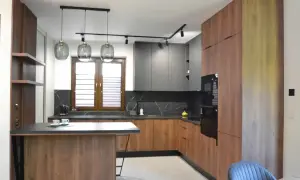 Nowoczesna kuchnia z wyspą otwarta na salon. Drewniane fronty szafek i szare, matowe górne szafki tworzą stylowe połączenie.