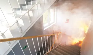 Rauch und Flammen im Treppenhaus eines Mehrfamilienhauses. Ein Feuerlöscher hängt an der Wand. Beachten Sie die Brandschutzvorschriften im Treppenhaus.