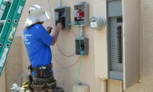 Elektryk pracuje przy skrzynce elektrycznej, podłączając przewody. To kluczowy etap instalacji, który zapewni odpowiednią moc przyłączeniową.