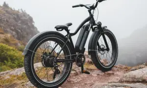 Czarny rower elektryczny z grubymi oponami na skalistym podłożu. Idealny do trudnego terenu, mógłby znaleźć się w czołówce rankingu rowerów elektrycznych.