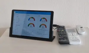 Tablet z systemem Linux wyświetla dane o temperaturze i wilgotności. Obok leżą piloty.