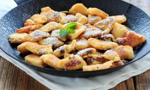Ein frisch zubereiteter Kaiserschmarrn in Wien, bestäubt mit Puderzucker und garniert mit Minze, serviert in einer Pfanne.