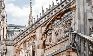 Gotycka architektura Duomo, z której słynie Mediolan, z detalami rzeźb i iglicami na tle błękitnego nieba.